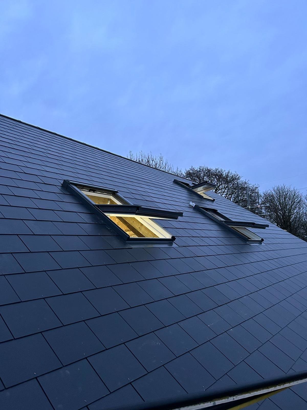 New slate roof with three roof windows lit up at dusk